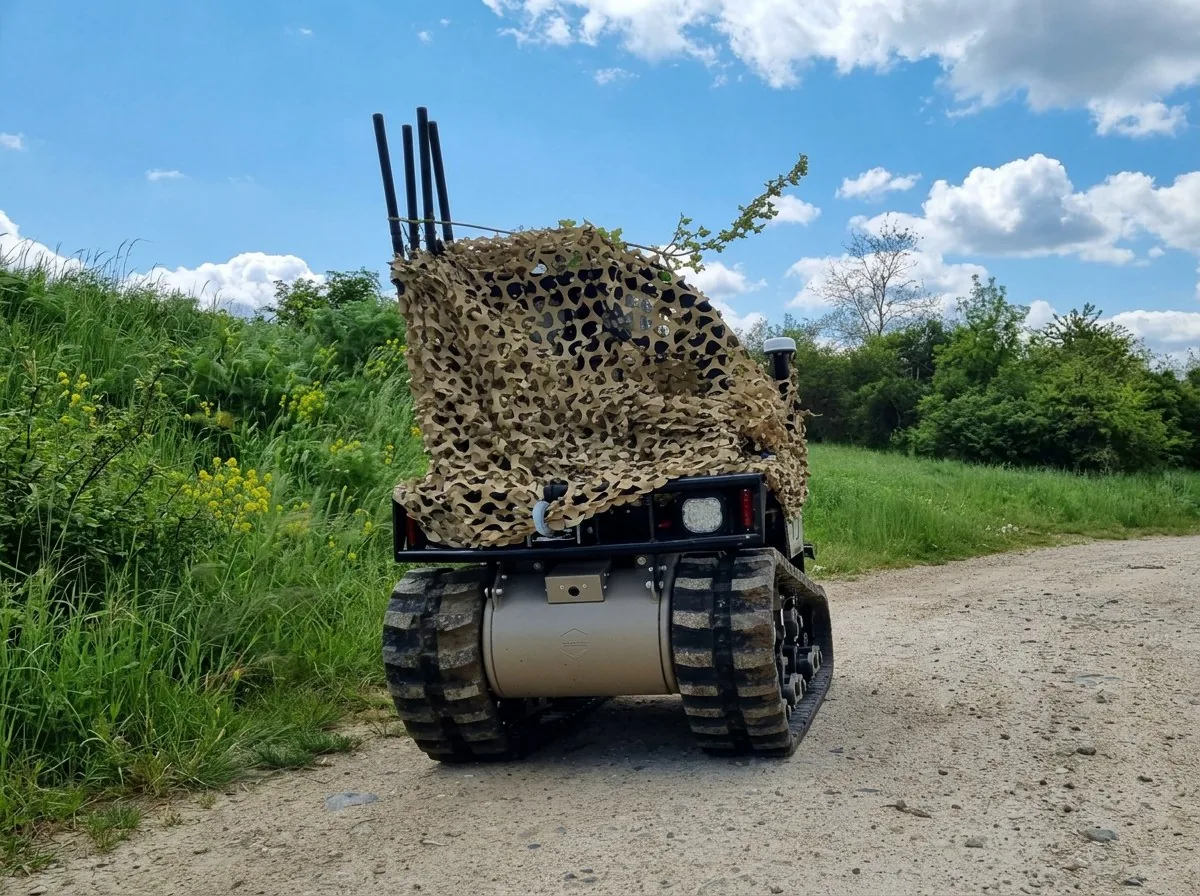 MAX1 under camouflage netting beside a dirt road